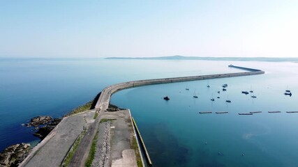 Sunny Holyhead harbour breakwater maritime yachts docked along transparent calm blue shoreline aerial slow right view