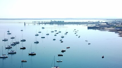 Sunny Holyhead harbour breakwater maritime yachts docked along transparent calm blue shoreline aerial flyover view