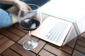 Glass of red wine stands on floor next to man sits in background