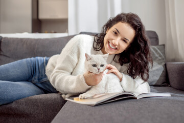 Cute woman laying on the sofa and caressing her cute white cat