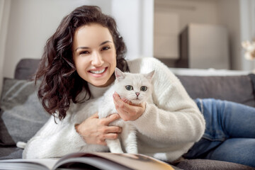 Cute woman laying on the sofa and caressing her cute white cat