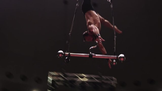 Training in circus - an acrobatic man standing upside down without hands and legs on the construction for the show in the air