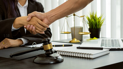 Obraz premium Counseling lawyer shakes hands with businessman in office with judge hammer and judge scale with laptop lawyer concept and legal advisor