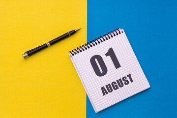 August 1st. Day of 1 month, calendar date. A notebook with a spiral and a pen lies on a yellow-blue background, flat lay, copy space