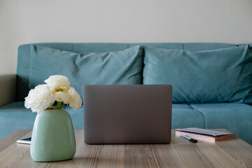 Home office concept. Designated work from home area in living room. Modern laptop, cellphone, notebook and vase with flowers on wooden table. Close up, copy space, background.