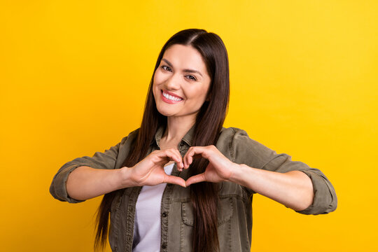 Photo of cheerful nice adorable young woman make fingers heart shape isolated on yellow color background