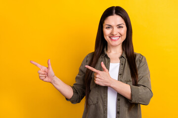 Photo of cheerful young charming woman point fingers empty space indicate news isolated on yellow...