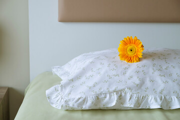 Close up shot of single orange gerbera flower on an unmade bed. Copy space for text, top view, background.