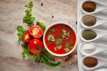 Close-up of Indian Homemade fresh and healthy tomato soup garnished with fresh coriander leaves and ingredients and herbs,  served in a white ceramic bowl with seasoning spices.