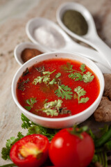 Close-up of Indian Homemade fresh and healthy tomato soup garnished with fresh coriander leaves and ingredients and herbs,  served in a white ceramic bowl with seasoning spices.