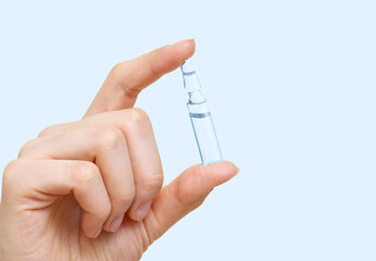 Medical ampoule for injection in female hand on a light blue background