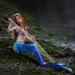Red-haired girl with a blue mermaid tail entangled in a fishing net