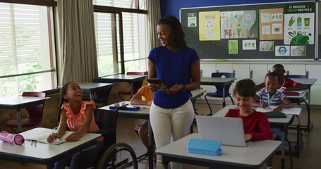 Happy diverse female teacher with tablet and schoolchildren during lesson in classroom - Powered by Adobe