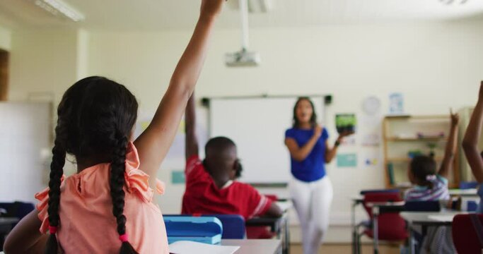 Mixed race female teacher standing in classroom asking questions abount plant during biology lesson