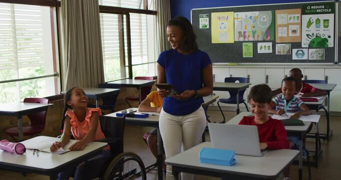 Happy diverse female teacher with tablet and schoolchildren during lesson in classroom