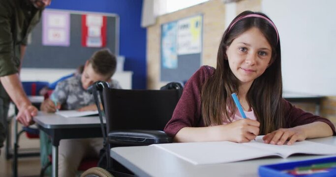 Portrait of happy caucasian schoolgirl sitting in wheelchair in classroom looking at camera