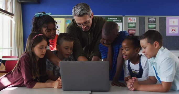 Diverse male teacher and group of schoolchildren looking at laptop