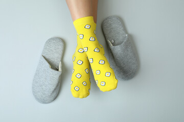 Female legs in funny socks on gray background with slippers