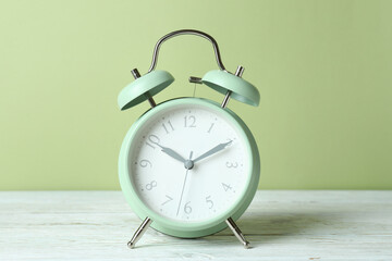 Alarm clock on white wooden table against green background