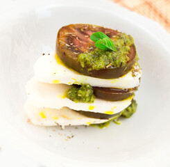 caprese salad with mozzarella, black tomatoes and pesto in white plate