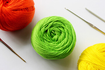 Crochet yarn background. Yarns green, red, yellow colors on white background with crochet hooks. Knitting, crochet supplies. Colorful cotton yarn for knitting. Handmade crocheting crafts, green yarn.