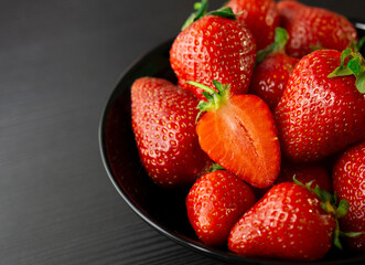 Red ripe strawberries in the black bowl on the dark background. Close up, top view. Ripe berries shot with copy space. Cut strawberry. 