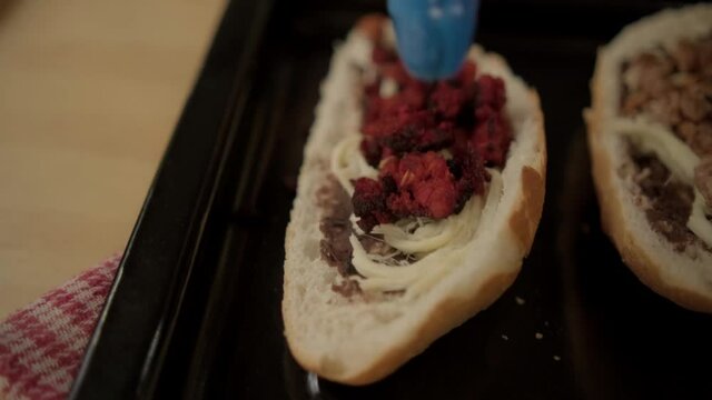 Blue tongs adding chopped meat to traditional Mexican molletes above black tray