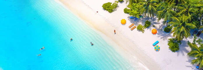 Beautiful summer tropical beach with white sand, palm trees, turquoise ocean water and tourists swimming in clear transparent  turquoise water. Panoramic aerial view. Ultra-wide background image.