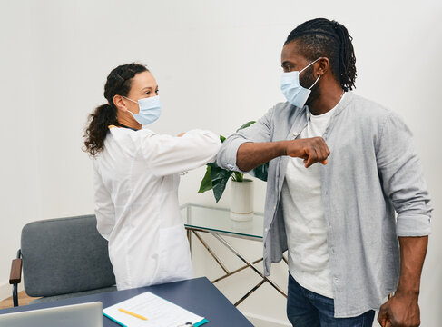 African American Man And His Doctor Wearing Medical Masks Greeting Each Other By Elbow Bumping At Doctor's Office. Elbow Bump, Battle Coronavirus Epidemic