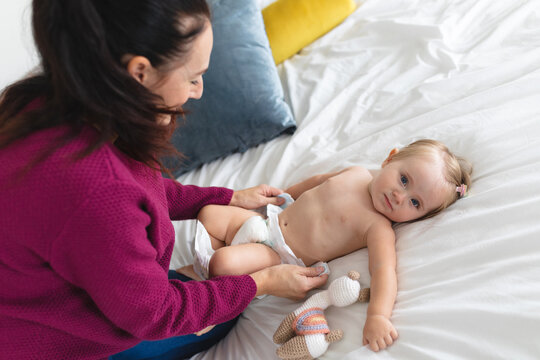 Caucasian mother changing diapers of her baby on the bed at home
