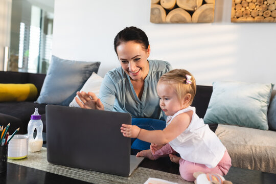 Smiling caucasian mother and her baby looking at laptop at home