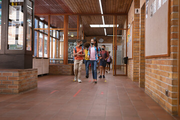 Group of diverse students wearing face masks walking in the corridor at school