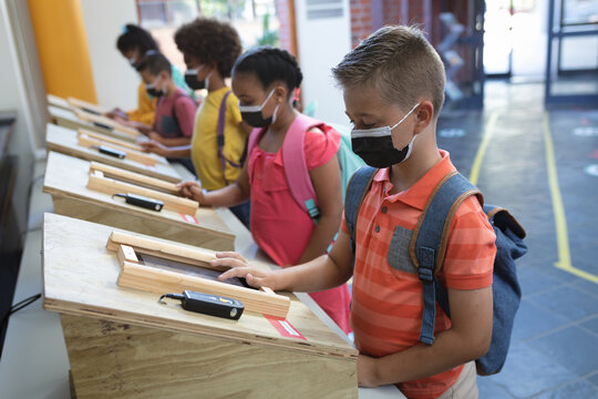 Group Of Diverse Students Wearing Face Masks Using Digital Tablets At School