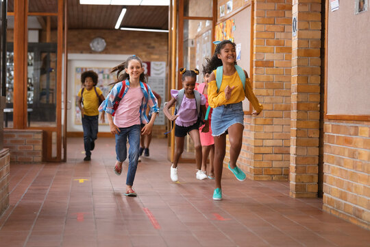 Group of diverse students running together in the corridor at school