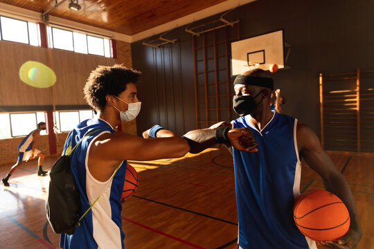 Diverse male basketball team greeting with elbows and wearing face masks - Powered by Adobe