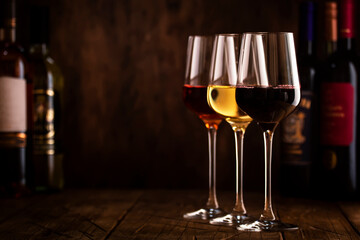 Wine tasting. Red, white and rose wine in glasses on wooden background in rustic cellar or bar with collection of wine bottles, frame with copy space