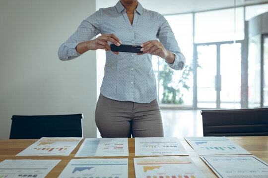 Mixed race businesswoman taking photo of documents on desk with smartphone
