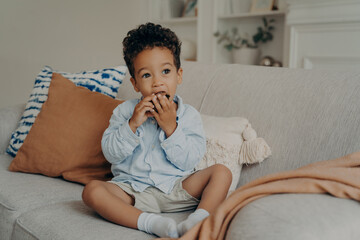 Fototapeta na wymiar Hungry cute afro american boy eating cupcake while spending time at home