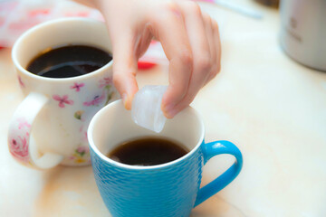 The girl throws ice into the mug to cool the drink.