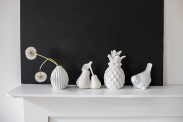 White figurines of pineapple, pear, bird, a vase with two dandelions on the background of a black...