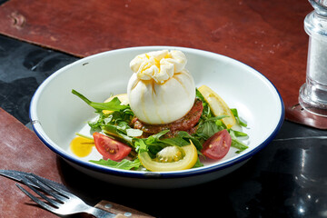 Salad with mozzarella burrata, arugula, pesto, cherry tomatoes in a white plate. Dark background. Hard light