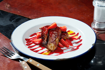 Fried foie gras liver with berry sauce and strawberries in a white plate. Dark background. Hard...