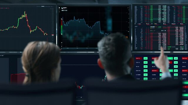Colleagues traders are working with multiple computer screens full of charts and data analysis and stock broker trading online. Back view. Concept of bitcoin and stock market trading.