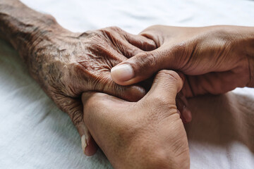 .Hands of the old man and a man hand on the white bed