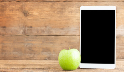 Education concept. The tablet with black screen and green apple on a wooden background.