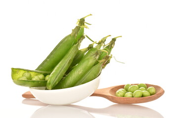 Several organic green pea pods in a white ceramic saucer with a wooden spoon, close-up, isolated on white.