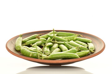 Several organic green pea pods on a plate of clay, close-up, isolated on white.