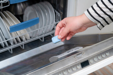 Close up of hand inserting soap capsule into dish washer in the kitchen. Person putting dish...
