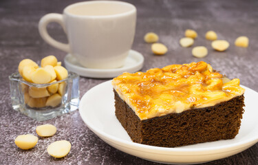 Toffee chocolate cake slice on plate with macadamia seeds and coffee cup on stone background for dessert break
