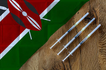 Concept of the ongoing efforts by Kenya to deliver and distribute COVID-19 vaccines with three syringes on a wooden table ready to use with a Kenyan Flag. Copy Space for Text and Graphics.